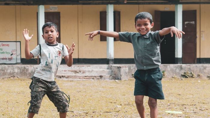 Two children playing joyfully outdoors at a rural Assam schoolyard